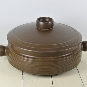 May include: A brown ceramic casserole dish with a lid and two handles. The dish has a ridged design and a small knob on the lid.
