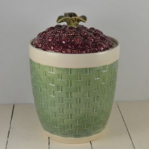 May include: A green ceramic cookie jar with a woven pattern and a lid shaped like a cluster of red raspberries.