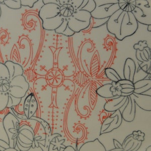 May include: A white ceramic plate with a black and red floral design. The design features a large red floral pattern in the center of the plate, surrounded by smaller black floral patterns.