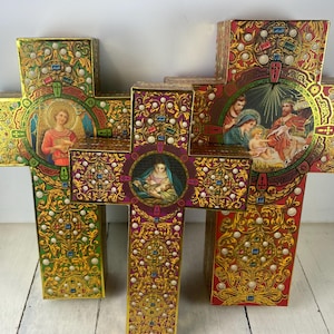 May include: Several decorative crosses with ornate gold, green, and red designs. Each cross features religious imagery, including angels and biblical scenes. The crosses are embellished with pearl-like accents and intricate patterns.