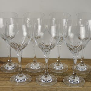 May include: A set of eight clear crystal wine glasses. Each glass has a long stem, a round base, and a bowl-shaped top. The glasses are arranged on a wooden surface, showcasing their elegant design and clarity. Ideal for serving wine.