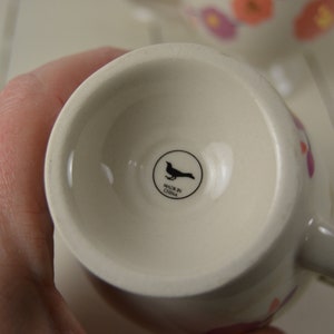 May include: White ceramic mug with a floral design and a black bird logo that says "Made in China".