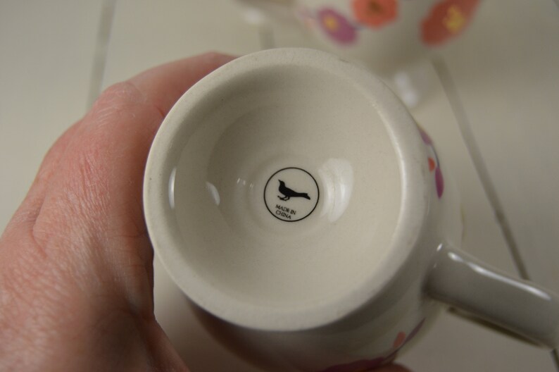 May include: White ceramic mug with a floral design and a black bird logo that says "Made in China".