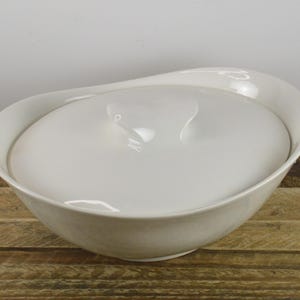 May include: White ceramic serving bowl with a lid. The bowl has a rounded, organic shape.
