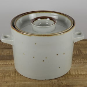 May include: A white ceramic crock with a brown rim and lid. The crock has a speckled brown glaze and two handles.