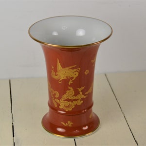May include: A red ceramic vase with a gold dragon and cloud design. The vase has a wide mouth and a narrow base.