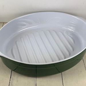 May include: Oval-shaped, green and white enamel baking dish. The dish has a white interior with ridged bottom and a green exterior. It features two handles and is suitable for baking and serving.