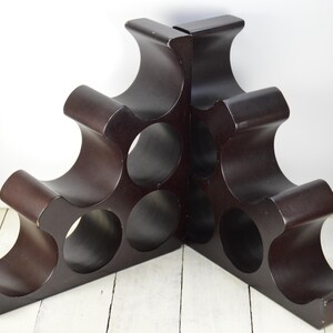 May include: A dark brown wooden wine rack with a unique, wave-like design. The rack holds six bottles of wine.