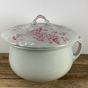 May include: A white ceramic chamber pot with a matching lid. The lid and pot feature a floral pattern in shades of red. The pot has a handle on the side and a loop handle on the lid.