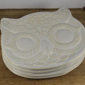 May include: Set of four white ceramic owl-shaped plates with gold accents. The plates are stacked on top of each other.