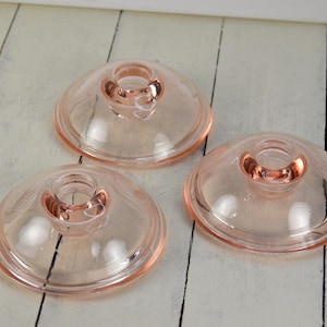 May include: Three pink glass candle holders with a clear glass center. The candle holders are round and have a raised rim.