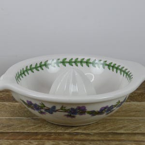May include: White ceramic citrus juicer with a green and purple floral design. The juicer has a ridged center for squeezing citrus fruits.