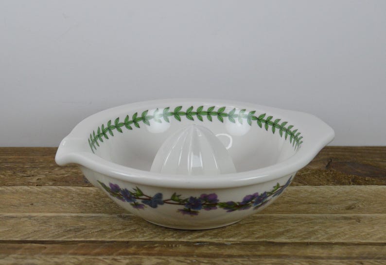 May include: White ceramic citrus juicer with a green and purple floral design. The juicer has a ridged center for squeezing citrus fruits.