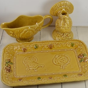May include: A yellow ceramic Thanksgiving serving set with a gravy boat, a turkey-shaped creamer, and a rectangular serving tray with two turkey designs.