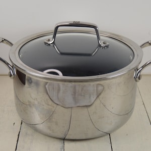 May include: A stainless steel pot with a glass lid. The pot has a silver finish and a black interior. The lid has a handle on top.