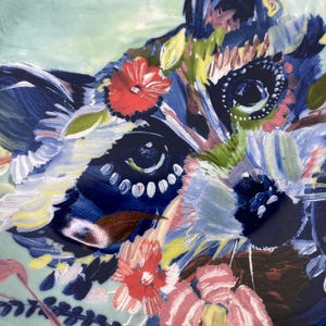 May include: A decorative ceramic plate featuring a colorful floral design with a raccoon face. The plate has a light blue background with red, pink, blue, and yellow flowers. The rim is gold.