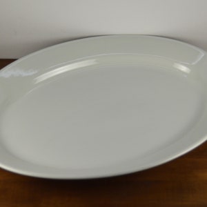 May include: A white oval serving platter with a slightly raised rim. The platter is made of ceramic and has a smooth, glossy finish.
