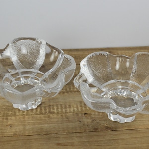 May include: Two clear glass bowls with a textured surface and a flower-like shape. The bowls have a small pedestal base.
