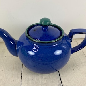 May include: A blue ceramic teapot with a rounded body, spout, and handle. The lid is topped with a green knob and has a green trim. The teapot is designed for brewing tea.