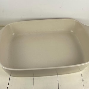 May include: A rectangular off-white ceramic baking dish with rounded corners and integrated handles on each side. The interior and exterior surfaces feature a subtle speckled texture throughout the light cream-colored finish of the bakeware.
