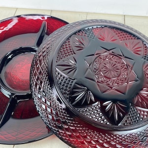May include: Two ruby red glass serving dishes. One is a divided serving platter with three sections. The other is a round serving bowl with a detailed starburst and diamond pattern. Both are vintage.