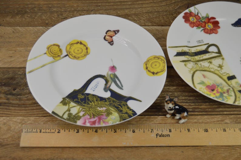 Puede incluir: Dos platos de cer&aacute;mica blanca con dise&ntilde;os florales y de mariposas. Los platos presentan un colibr&iacute;, flores amarillas y una mariposa. Los platos est&aacute;n sobre una superficie de madera.
