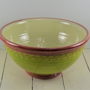 May include: A large ceramic bowl with a light green interior and a lime green exterior. The rim and base are a deep red-brown color. The exterior features a decorative pattern of red dots and lines.