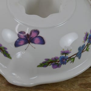 May include: White ceramic bowl with a floral design featuring purple and blue flowers and a pink butterfly. The bowl has a scalloped edge.