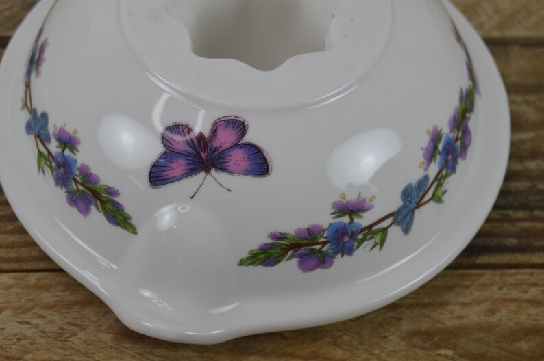 May include: White ceramic bowl with a floral design featuring purple and blue flowers and a pink butterfly. The bowl has a scalloped edge.