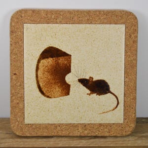 May include: Square cork coaster with a cream-colored tile center. The tile features a brown illustration of a mouse facing a cheese wedge. The coaster has a rustic, vintage aesthetic.