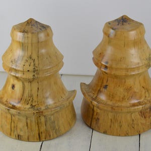 May include: Two wooden decorative objects with a layered, tiered design. The objects are made of light brown wood with dark brown streaks and are shaped like a pagoda.