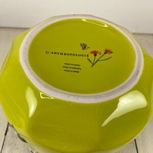 Może przedstawiać: Chartreuse ceramiczna miska z białym obramowaniem. Wnętrze miski zawiera napis "by ANTHROPOLOGIE" i mały kwiatowy wz&oacute;r. Sp&oacute;d miski jest oznaczony "Made in China" i "Hecho en China".