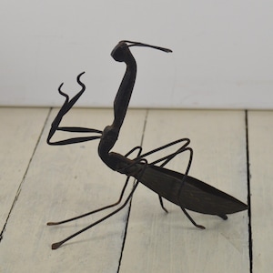 May include: A black metal sculpture of a praying mantis. The sculpture is made of thin metal and is very detailed. The mantis is posed with its front legs raised in a praying position.