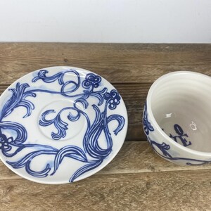 Puede incluir: Juego de taza y platillo de t&eacute; de cer&aacute;mica blanca con dise&ntilde;os florales azules. El platillo presenta un pozo central y un patr&oacute;n azul detallado. La taza tiene un asa y un dise&ntilde;o floral azul a juego.