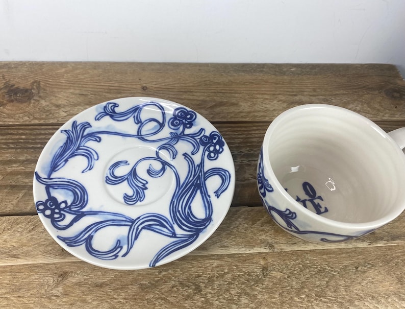 Puede incluir: Juego de taza y platillo de t&eacute; de cer&aacute;mica blanca con dise&ntilde;os florales azules. El platillo presenta un pozo central y un patr&oacute;n azul detallado. La taza tiene un asa y un dise&ntilde;o floral azul a juego.