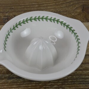 May include: White ceramic citrus juicer with a green leaf design around the rim. The juicer has a removable, white, cone-shaped reamer.