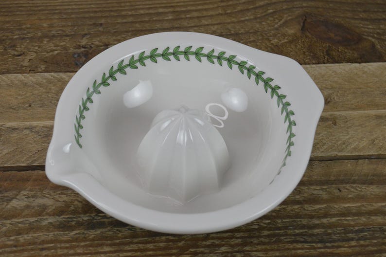 May include: White ceramic citrus juicer with a green leaf design around the rim. The juicer has a removable, white, cone-shaped reamer.