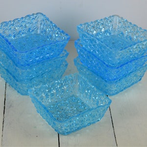 May include: A stack of eight light blue glass bowls with a textured, diamond-shaped pattern. The bowls are square and have a scalloped edge.