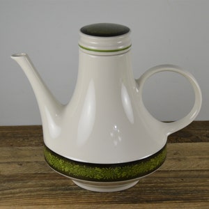 May include: White ceramic teapot with a green and brown floral design around the base. The teapot has a wide, round body and a tall, slender spout. The lid is green and brown with a white band.