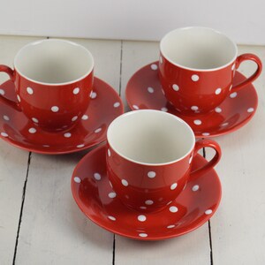 May include: Three red teacups with white polka dots and matching saucers. The cups and saucers are made of ceramic.