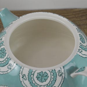 K&ouml;nnte beinhalten: Eine t&uuml;rkisfarbene Teekanne mit einem wei&szlig;en und t&uuml;rkisfarbenen Blumenmuster. Die Teekanne hat einen Deckel und einen Ausguss.