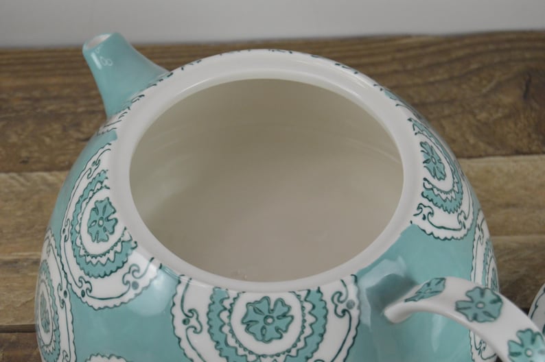 K&ouml;nnte beinhalten: Eine t&uuml;rkisfarbene Teekanne mit einem wei&szlig;en und t&uuml;rkisfarbenen Blumenmuster. Die Teekanne hat einen Deckel und einen Ausguss.
