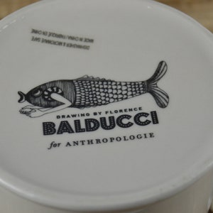 Pode incluir: Caneca de cer&acirc;mica branca com uma ilustra&ccedil;&atilde;o em preto e branco de um peixe com o texto "Drawing by Florence Balducci for Anthropologie" impresso na frente.