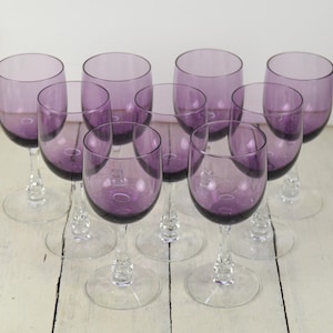 May include: Set of ten purple glass wine glasses with clear stems and bases. The glasses are arranged in two rows of five.