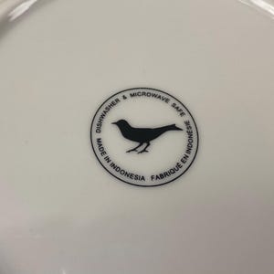 May include: White ceramic plate with a black bird silhouette in a circular design. Text around the bird reads "Dishwasher & Microwave Safe" and "Made in Indonesia Fabriqu&eacute; en Indon&eacute;sie".