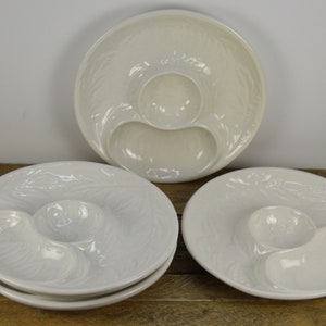 May include: Set of four white ceramic serving dishes with a raised design. Each dish has three sections, one large and two smaller.