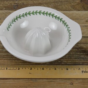 May include: White ceramic citrus juicer with a green leaf design around the rim. The juicer has a small, white, ridged cone in the center.