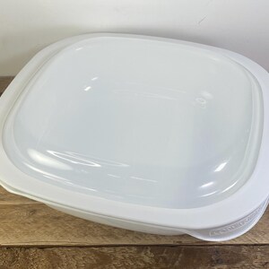 May include: A square white plastic food storage container with rounded corners and a matching translucent white lid. The container features a smooth, glossy finish and a simple design, with the brand name Correlle embossed on the side rim.