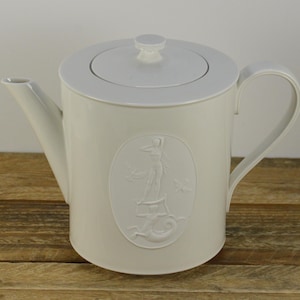May include: White ceramic teapot with a lid and a handle. The teapot has an embossed design of a woman standing on a pedestal with a mermaid tail.