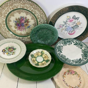 May include: A collection of seven ceramic plates and dishes featuring various designs, including floral patterns, gold filigree, a green cabbage-leaf textured plate, a solid dark green oval platter, and intricate green and white botanical motifs.